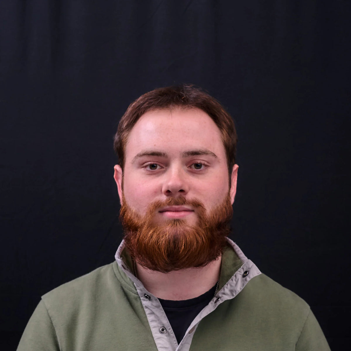 Man with a beard wearing a green jacket against a black background