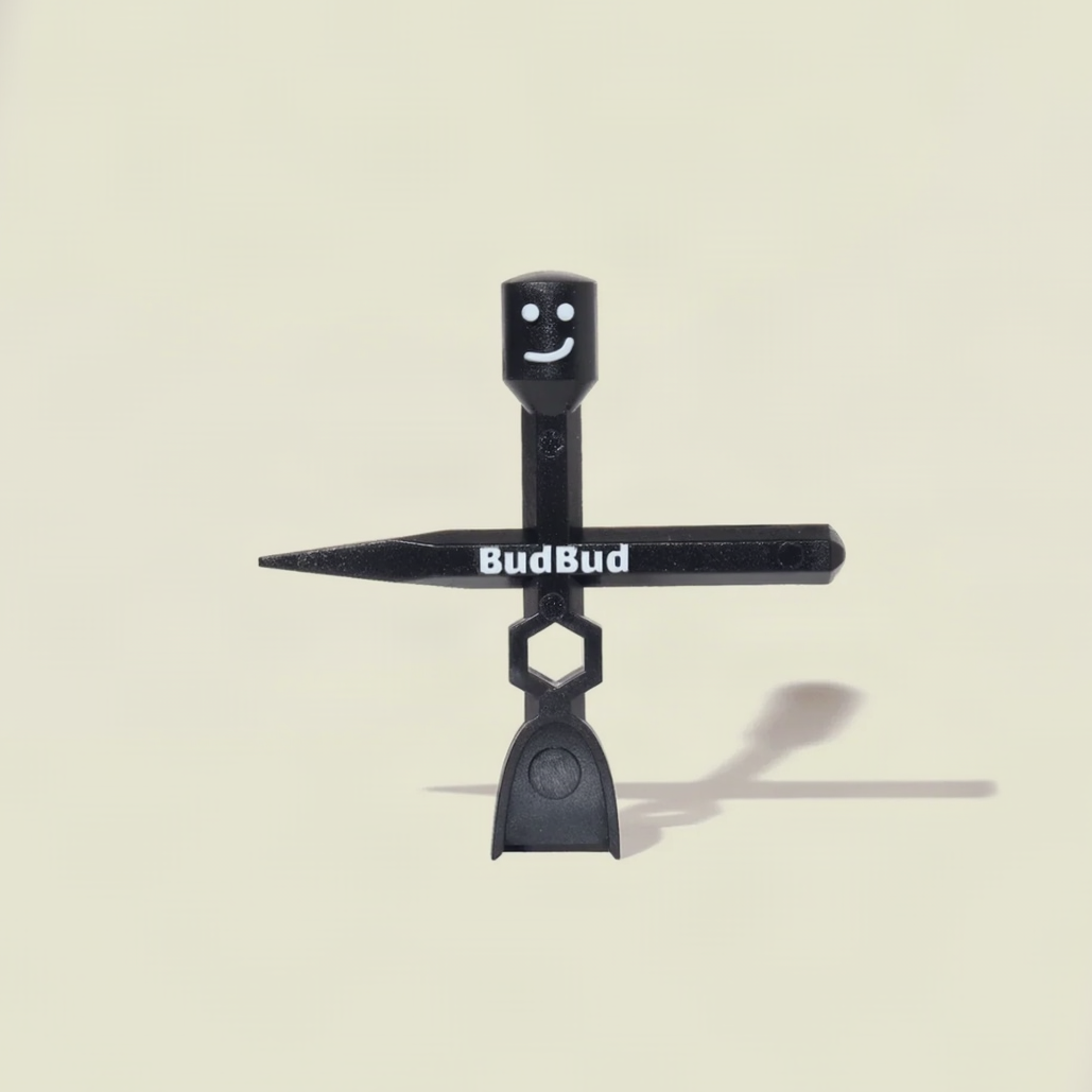 A black plastic BudBud flower stake with a smiling face on the top cone, white BudBud logo on the horizontal arm, and a hexagonal loop near the bottom, shown against a light beige background with a soft shadow.