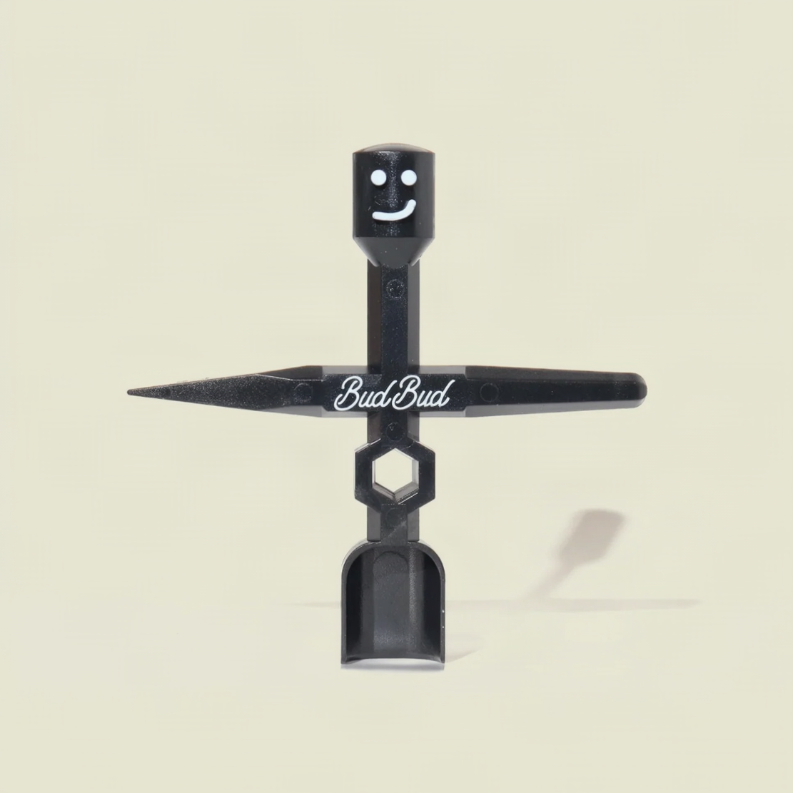 A black plastic BudBud brand tool with a smiling face on the top cap, a horizontal arm printed with the BudBud logo, and a scoop-like bottom section, photographed against a light beige background.