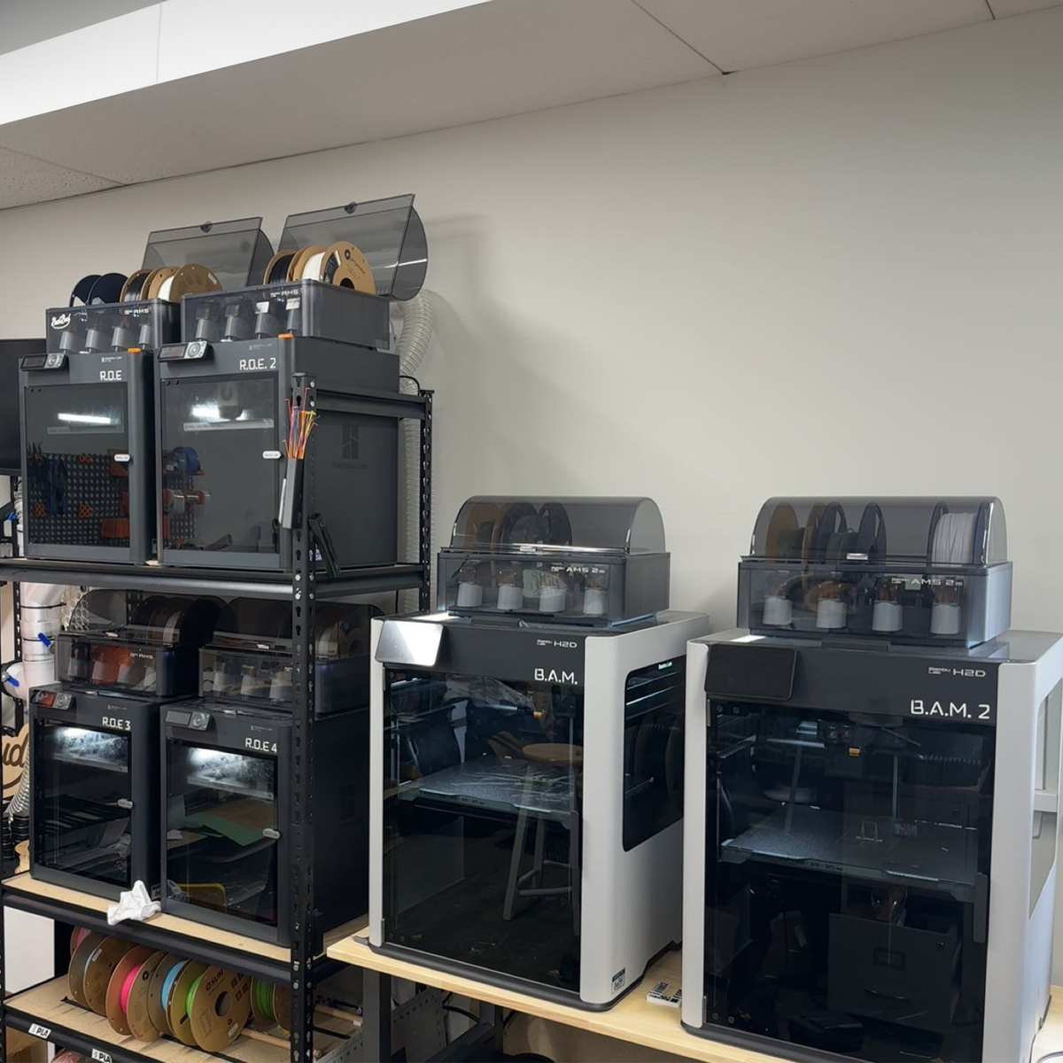 Multiple 3D printers on shelves in a room setting