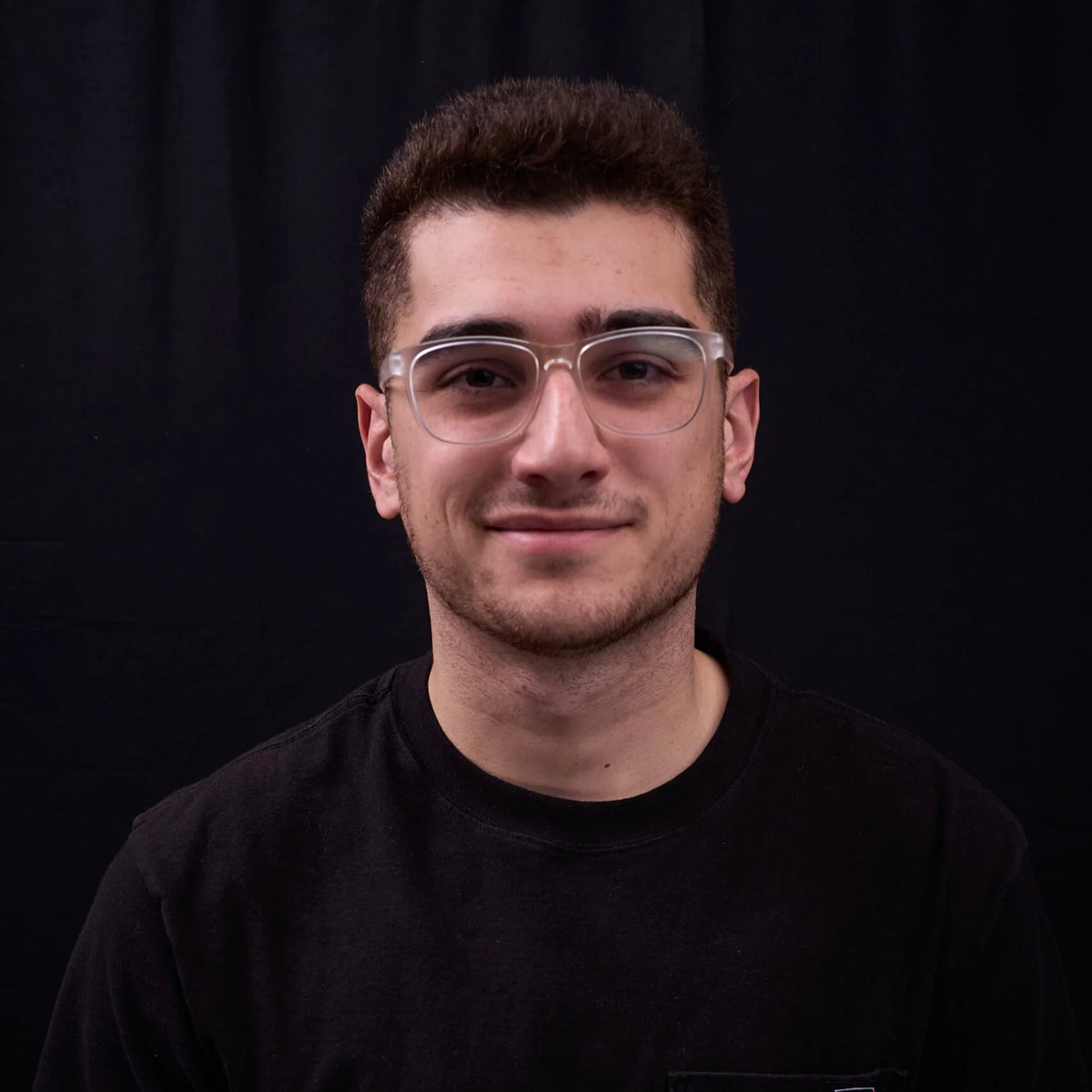 Man wearing glasses and a black shirt against a black background